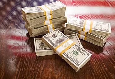 Thousands of dollars stacked with reflection of american flag on wooden table