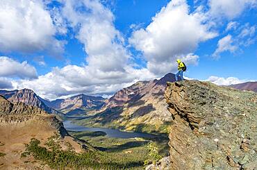 Hiker standing on rock ledge, view of Two Medicine Lake, mountain peaks Rising Wolf Mountain and Sinopah Mountain, hiking trail to Scenic Point, Glacier National Park, Montana, USA, North America