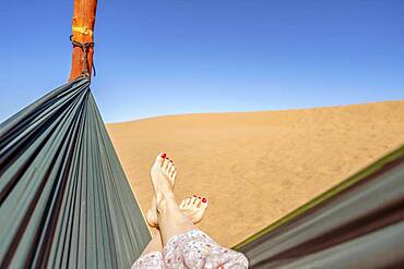 Young woman relaxing in green hammock with view on sand dunes of Sahara Desert, Morocco, Africa