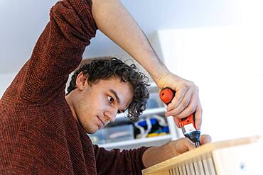 Young man doing DIY in his apartment, assembling a shelf