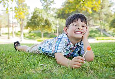 Handsome young boy enjoying his lollipop outdoors on the grass