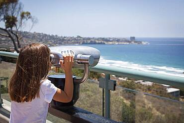 Young girl looking out over the pacific ocean and la jolla, california with telescope