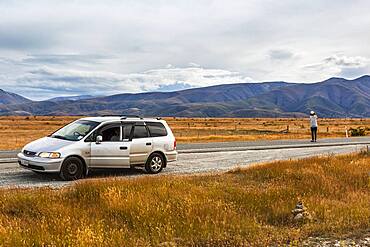 Guy with camera next to car, Omarama, Waitaki District, Canterbury, South Island, New Zealand, Oceania