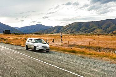 Guy with camera next to car, Omarama, Waitaki District, Canterbury, South Island, New Zealand, Oceania