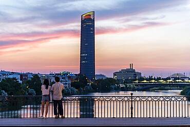 Couple standing on the bridge at sunset, Puente de Triana, view over the river Rio Guadalquivir, in the back skyscraper Torre Sevilla, Sevilla, Andalusia, Spain, Europe