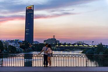 Couple standing on the bridge at sunset and kissing, Puente de Triana, view over the river Rio Guadalquivir, in the back skyscraper Torre Sevilla, Sevilla, Andalucia, Spain, Europe