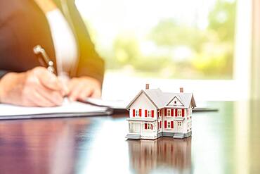 Woman signing real estate contract papers with small model home in front