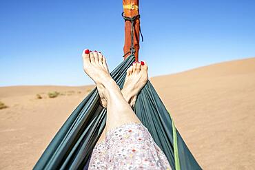 Young woman relaxing in green hammock with view on sand dunes of Sahara Desert, Morocco, Africa