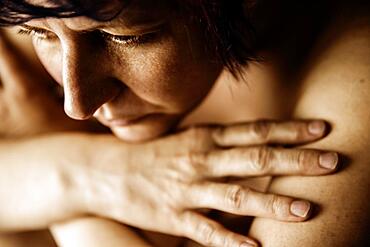 Naked sitting woman thoughtfully rests her head on her folded arms, studio shot, Germany, Europe