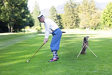 Older man in straw hat and knickerbockers playing hickory golf on a golf course