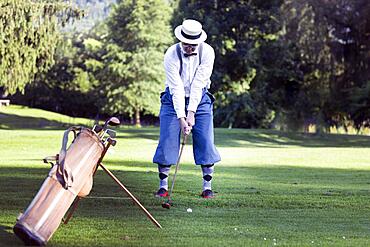 Older man in straw hat and knickerbockers playing hickory golf on a golf course