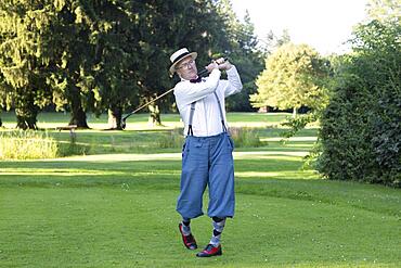 Older man in straw hat and knickerbockers playing hickory golf on a golf course