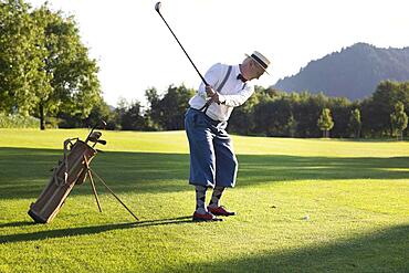 Older man in straw hat and knickerbockers playing hickory golf on a golf course