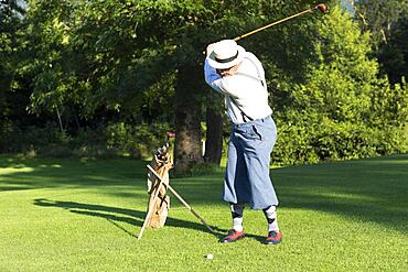 Older man in straw hat and knickerbockers playing hickory golf on a golf course