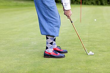 Older man in straw hat and knickerbockers playing hickory golf on a golf course