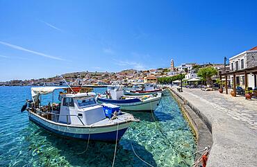 Fishing boats in the harbour of Halki with turquoise water, promenade with colourful houses of the village of Halki, Halki, Dodecanese, Greece, Europe