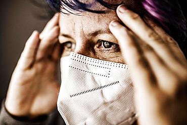 Woman with FFP2 medical mask looks thoughtful and holds hands to her head, studio shot, Germany, Europe