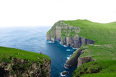 A person standing in the distance in front of Asmundarstakkur cliff, Sandvik, Suduroy, Faroe Islands, Europe