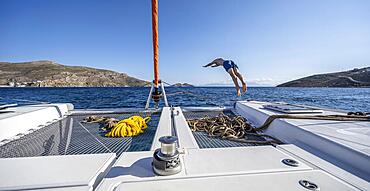 Young man jumps into the water, ropes on a sailing catamaran, sailing trip, Tilos, Dodecanese, Greece, Europe