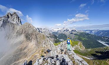 Hiker on a summit, Westliche Toerlspitze, mountains with dramatic clouds, middle Zugspitze, behind Patenkirchner Dreitorspitze, Wetterstein range, Garmisch-Partenkirchen, Bavaria, Germany, Europe