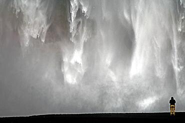 Man in front of falling masses of water, Skogafoss, South Iceland, Iceland, Europe