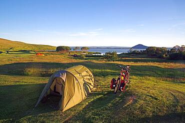 Tunnel tent and touring bike on spacious meadow, lake in the background, Myvatn, Iceland, Europe