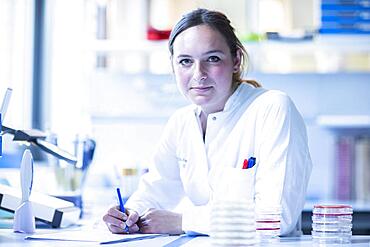 Young lab technician with sample on petridish working in a lab with lab equipment and protocol, Freiburg, Baden-Wuerttemberg, Germany, Europe