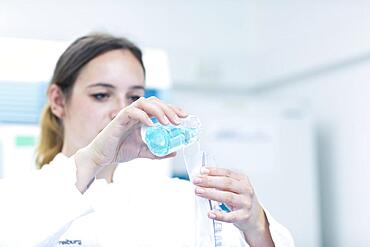 Young laboratory assistant with sample and laboratory glasses working in a laboratory with laboratory equipment, Freiburg, Baden-Wuerttemberg, Germany, Europe