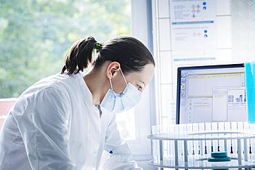 Young chemist with sample and laboratory glasses working in a laboratory with laboratory equipment and monitor, Freiburg, Baden-Wuerttemberg, Germany, Europe