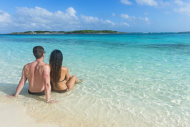 Couple sitting on a white sand beach in the turquoise waters of the Exumas, Bahamas, Caribbean, Central America