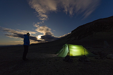 Man with headlamp standing in front of tent lit from inside, moonrise, Askja volcano, Icelandic highlands, Iceland, Europe