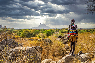 Traditional dressed young girl from the Laarim tribe standing on a rock, Boya hills, Eastern Equatoria, South Sudan, Africa