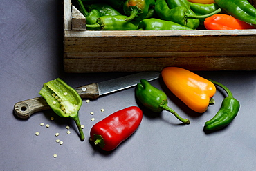 Different coloured peperonis in box and opened pod with knife, parika