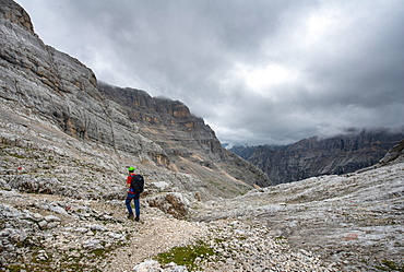 Hiker, climber on a trail between rocky cloudy mountains at Forcella Sore de la Cengia, Sorapiss circumnavigation, Dolomites, Belluno, Italy, Europe