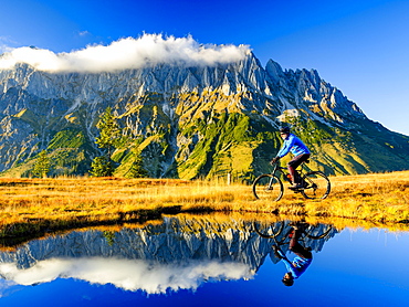 Mountain biker in front of mountain scenery reflected in a mountain lake, Mandlwand, Hochkoenig, Berchtesgaden Alps, Muehlbach am Hochkoenig, Pongau, Salzburg, Austria, Europe