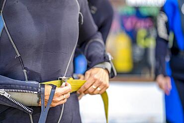 Woman wearing scuba diving weights before going underwater, Spain, Europe