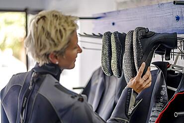 Blond woman in wetsuit choosing boots for water adventure, Spain, Europe