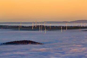 Wind turbines illuminated by the sun and forest rising from cloud cover, sunset, Koeterberg, Luegde, Weserbergland, North Rhine-Westphalia, Germany, Europe