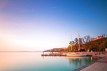 Shore at a lake, with boats. In the background is the abbey, church of Tihany and the sun is rising, Balaton, Lake Balaton, Hungary, Europe