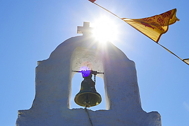 White bell tower, close-up, sky blue and cloudless, Pentecost service, Agias Triadas Chapel, backlight, sun as star, Orthodox flags, near Korfi, Andros Island, Cyclades, Greece, Europe