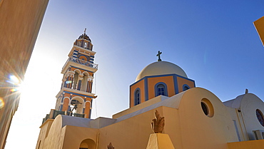 Soft morning light, wide angle, sun star-shaped next to church tower, St. John the Baptist Catholic Cathedral, blue, sandy and ochre, sky intense blue without clouds, Fira, Santorini Island, Cyclades, Greece, Europe