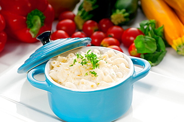 Macaroni and cheese, kids favourite dish, on a blue little childish clay pot with vegetables on background