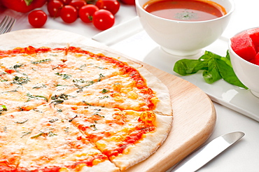 Italian original thin crust pizza Margherita with gazpacho soup and watermelon on side, and vegetables on background