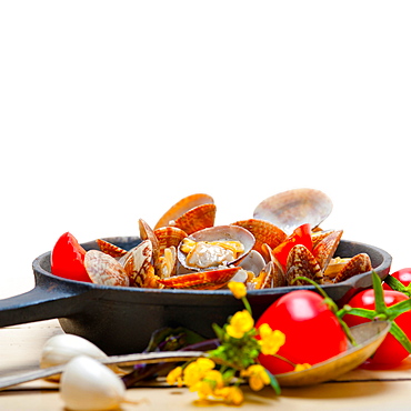 Fresh clams stewed on an iron skillet over wite rustic wood table