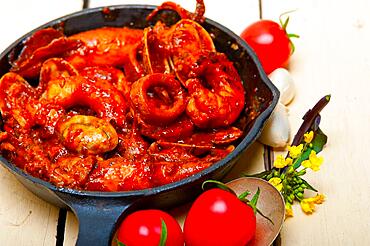 Fresh seafood stew prepared on an iron skillet ove white rustic wood table