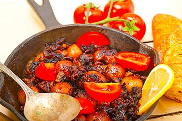 Baby cuttle fish roasted on iron skillet with tomatoes and onions over rustic wood table