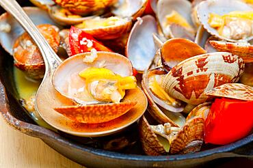 Fresh clams stewed on an iron skillet over wite rustic wood table