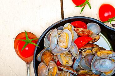 Fresh clams stewed on an iron skillet over wite rustic wood table