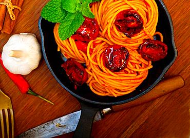 Italian spaghetti pasta and tomato with mint leaves on iron skillet over wood board