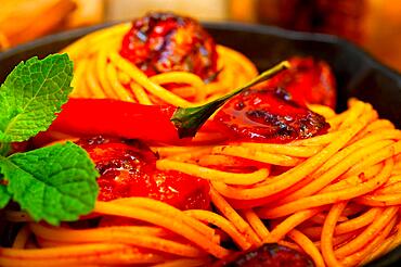 Italian spaghetti pasta and tomato with mint leaves on iron skillet over wood board